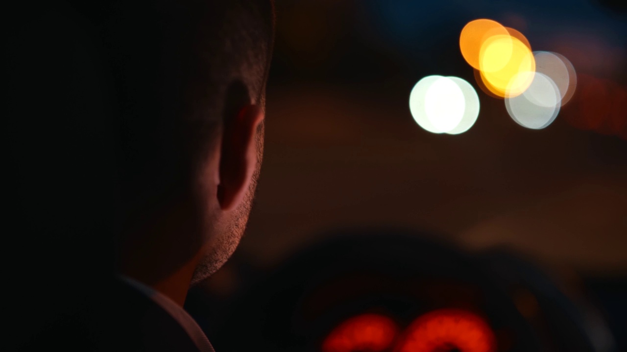 后面的成年男子司机开车，看着道路在晚上。关闭了。商人在晚上开车的背影。奢华的风格，模糊的背景视频素材