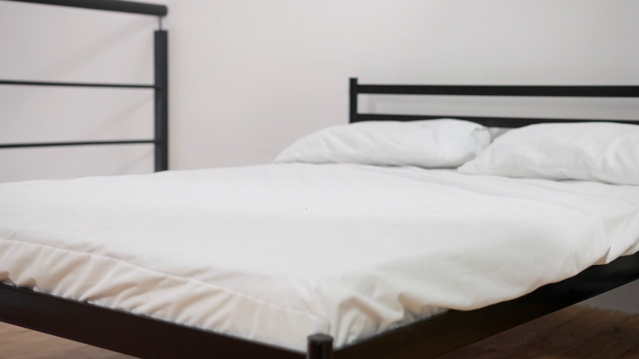 白色干净的毯子落在舒适的床上，在室内的慢动作。宽镜头舒适的卧室，柔软的床上用品在家里或酒店。豪华舒适的概念。视频素材