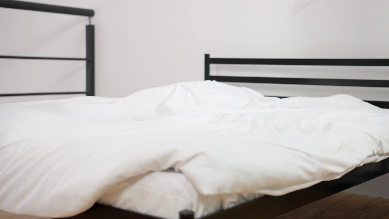 舒适的床在酒店的卧室与白色柔软的枕头落下在慢动作。室内宽敞舒适的家具。休闲和放松的概念。视频素材