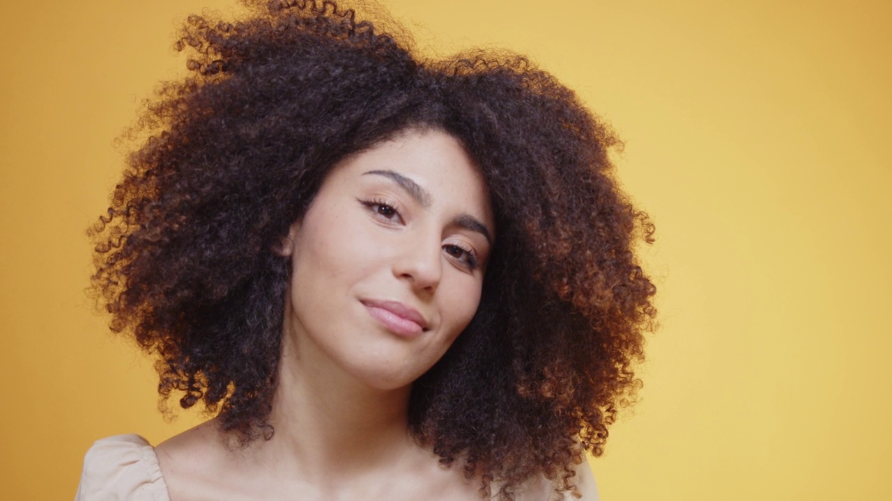 一位年轻的成年女性在橘黄色的背景下整理她的头发视频素材