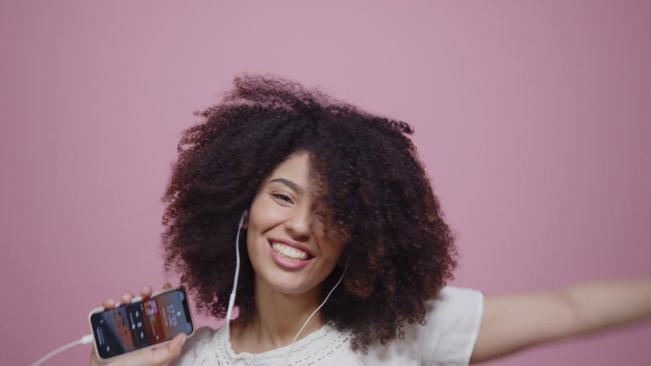 年轻的成年女子戴着耳机在粉红色的背景下跳舞视频素材