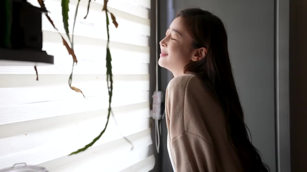 生活方式——年轻女子坐在窗边，休息，在家里微笑视频下载