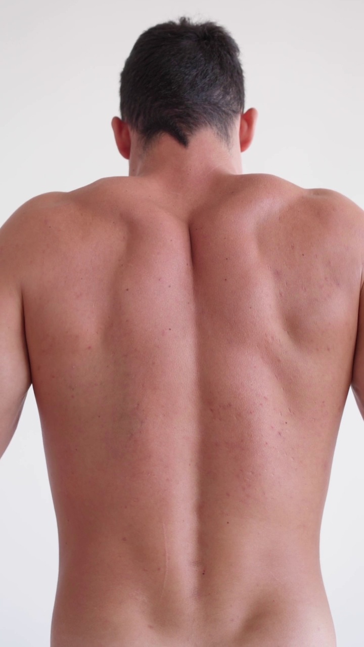 垂直视频运动员患有背痛。白底上的裸背。身体和皮肤护理的概念。颗粒男性皮肤视频下载