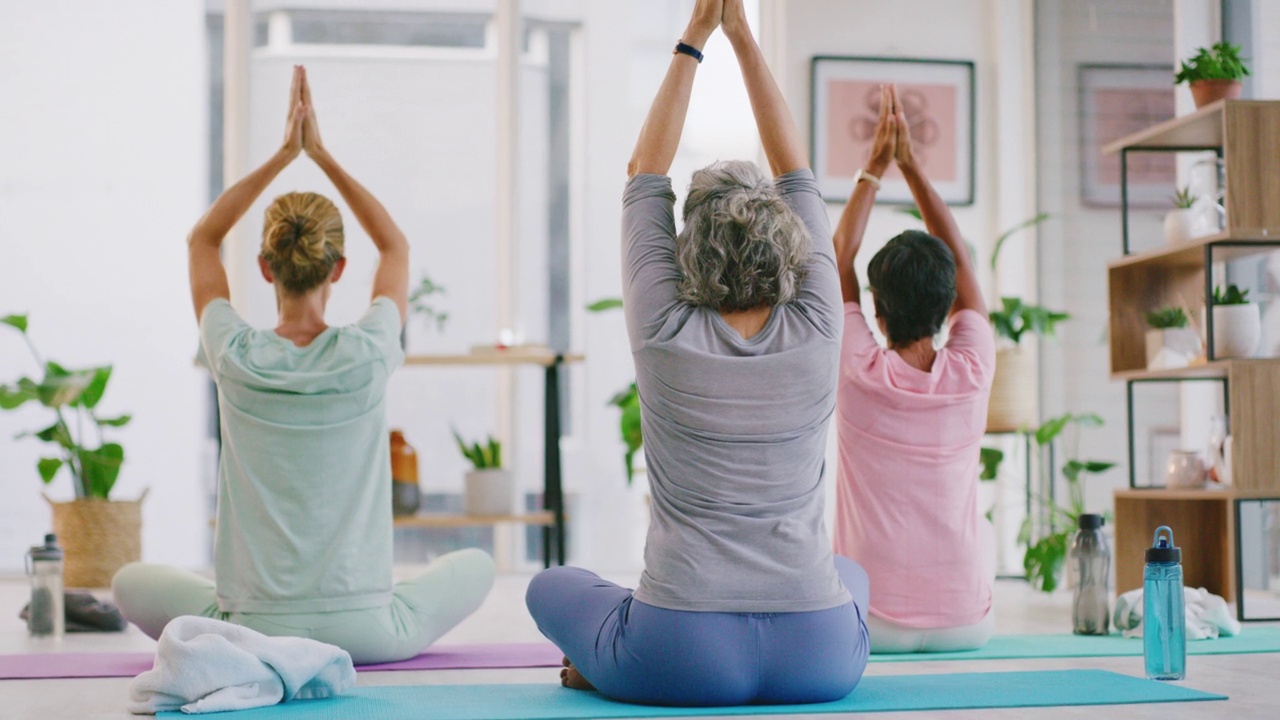 成熟的女性在禅瑜伽课上举起祈祷的手冥想。不同群体的瑜伽士坐在垫子上，双腿交叉，寻找内心的平衡或和平。练习镇静呼吸练习视频素材