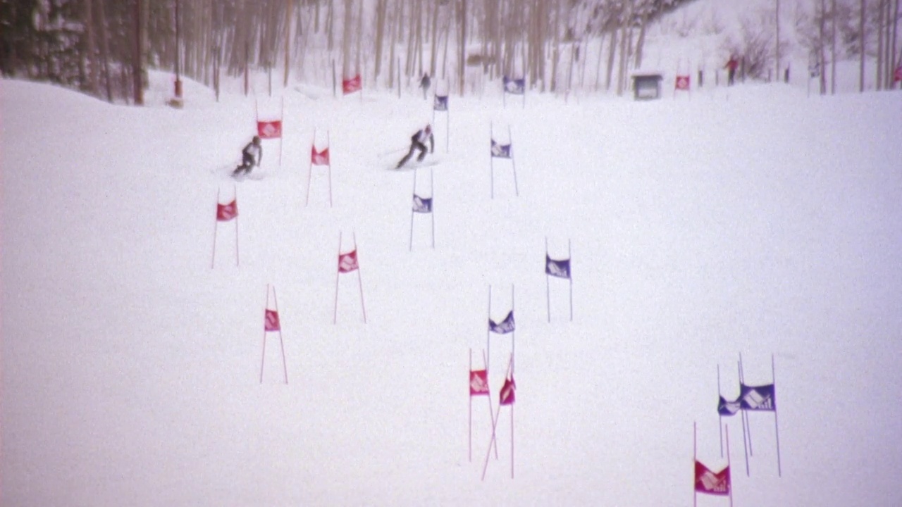 两个滑雪者在滑雪场滑雪下山的中角跟踪镜头。滑雪者从雪山上的旗子中滑下。滑雪者到达山脚的尽头。人群在国视频下载