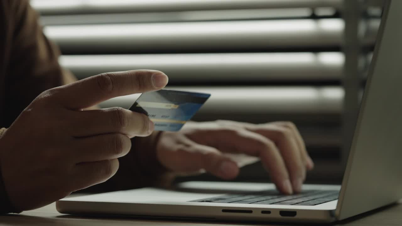 商人手里拿着信用卡，在家里用笔记本电脑网购。商人用小型笔记本电脑和银行卡在网上购物。视频素材