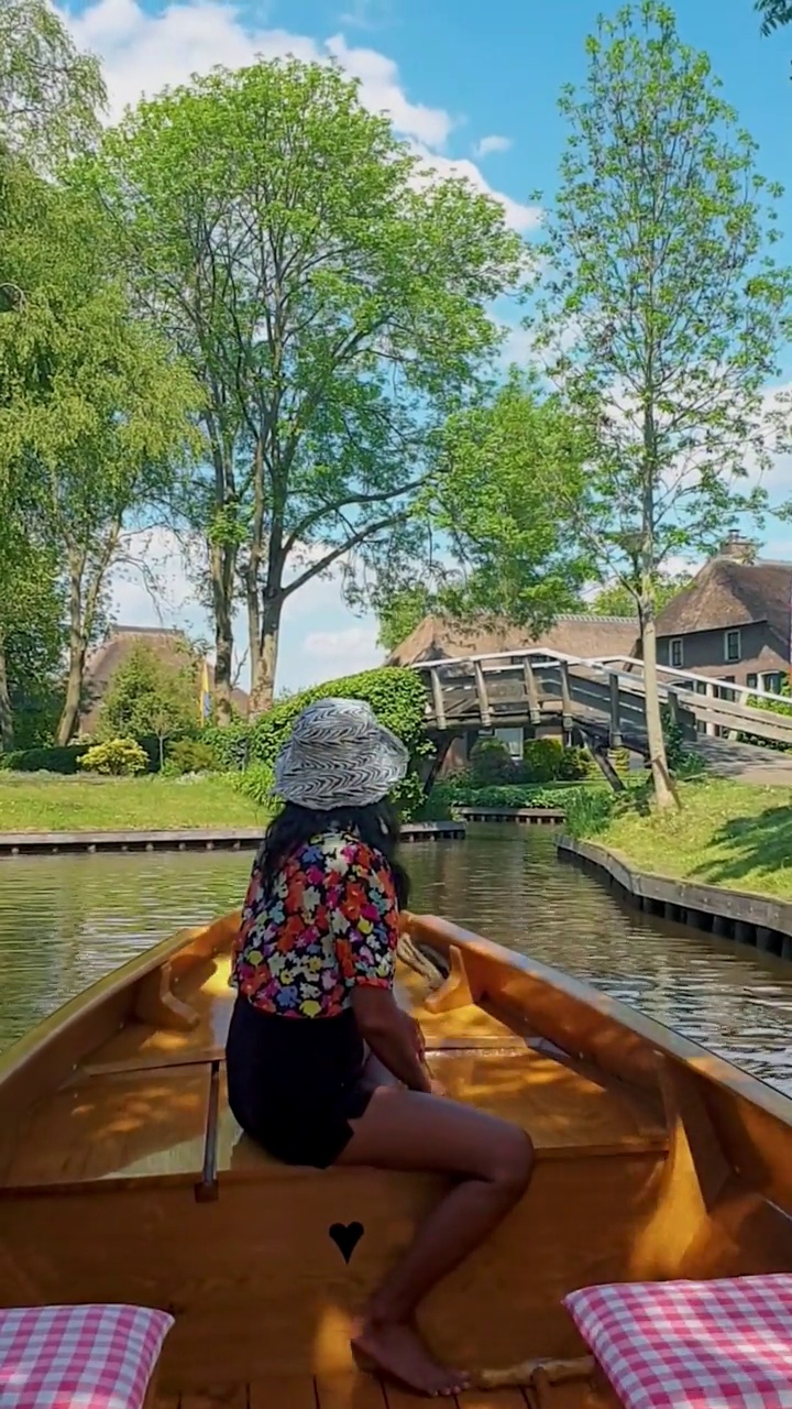 在荷兰基索恩运河的木船上戴着帽子的亚洲妇女。荷兰，基索恩:可以看到著名的基索恩村庄，那里有运河和质朴的茅草屋顶房屋视频素材