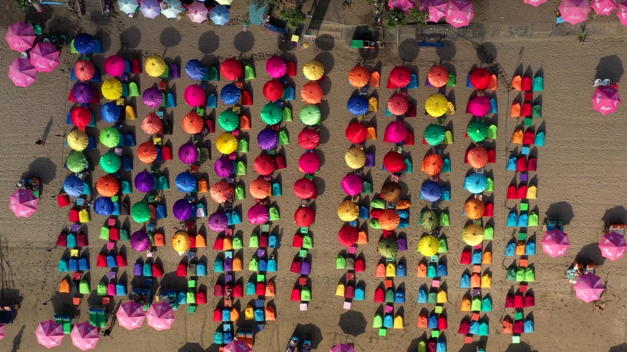从空中向上拍摄的人们在沙滩上的彩色阳伞下的豆袋度假-巴厘岛，印度尼西亚视频素材