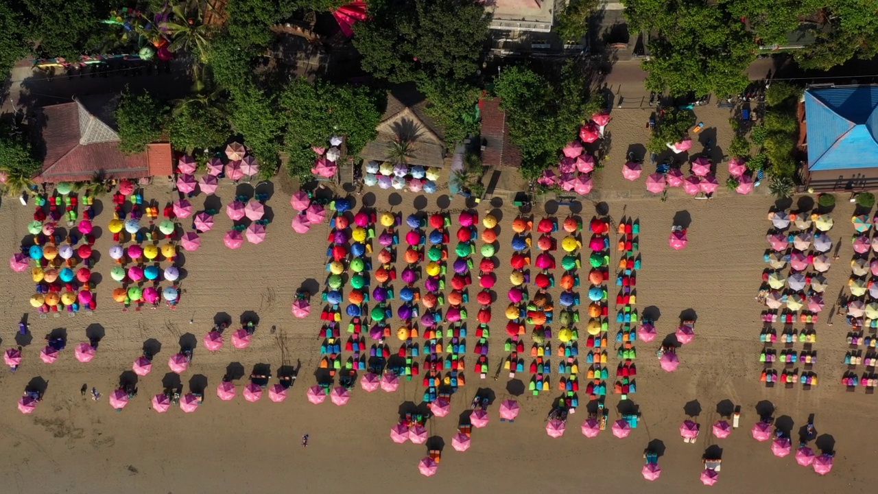 空中拍摄的彩色豆袋伞下的海滩，无人机在阳光明媚的日子向下飞行-巴厘岛，印度尼西亚视频下载