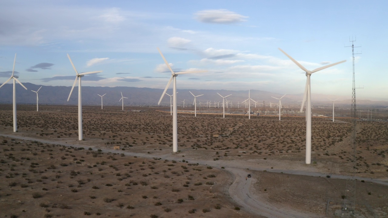 在多云的天空下，风力涡轮机在沙漠景观上旋转的空中向后拍摄-加州棕榈泉视频素材