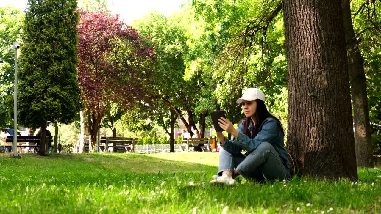 女人坐在夏日公园的树下看书视频下载