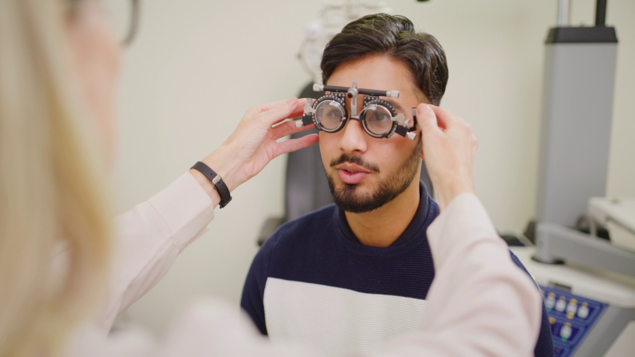 验光师在会诊处为男性病人做视力检查。女眼科医生使用眼镜框架与调整检查视力的一个年轻的印度男子。眼镜使用的跟踪框架视频下载
