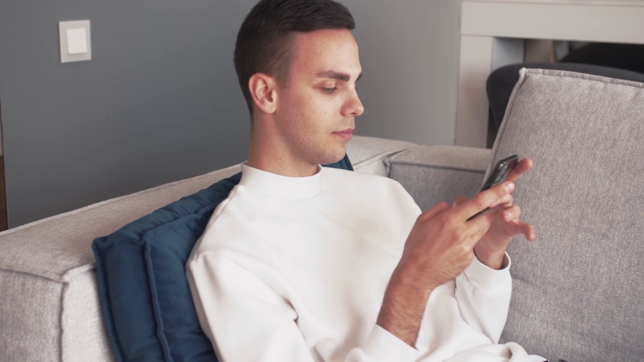 年轻的白人男子在家里的沙发上用手机放松视频素材