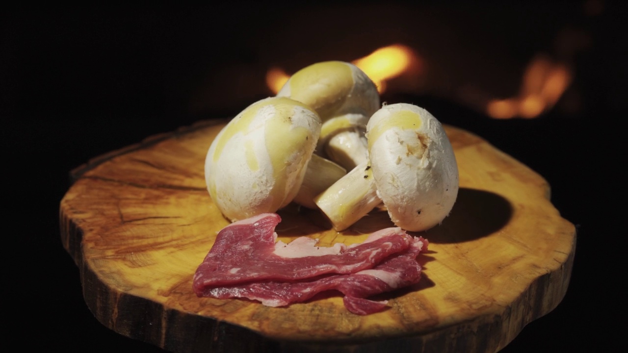 三个香菇放在一个木托盘上。旋转背景火，橄榄油，放培根。视频下载