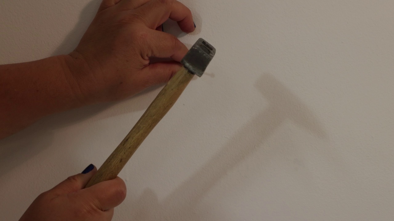 成年女性的手用力地把一颗钉子钉进一堵白墙里视频下载