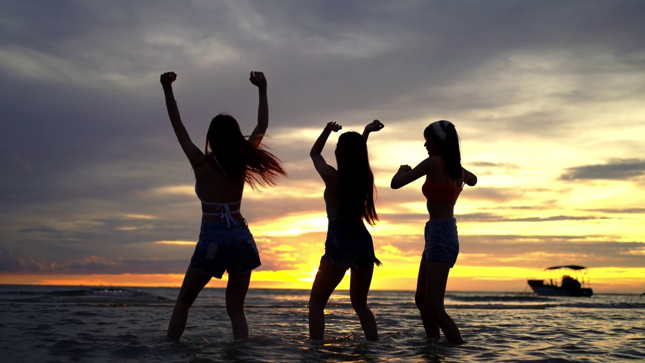 4K剪影一群亚洲女子在夏日夕阳下的热带海岛海滩上跳舞。视频下载