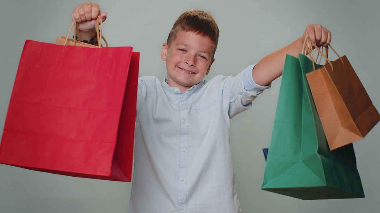 蹒跚学步的男孩展示购物袋，广告折扣，微笑着对低价感到惊讶视频素材