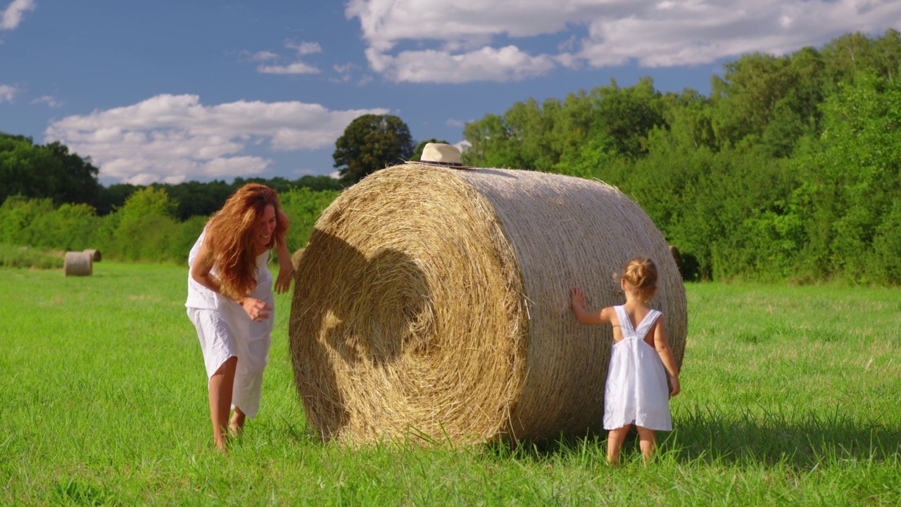 可爱的小女孩和她穿着白色连衣裙的妈妈在绿色的草地上微笑。母亲和孩子享受美丽的自然和太阳在日落时间一起在慢动作拍摄视频下载