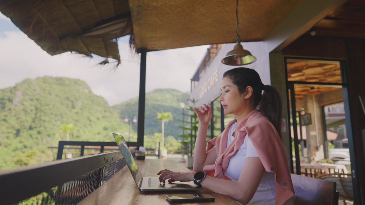 自由数字游牧民网页设计和开发微笑坐在咖啡馆使用笔记本电脑，而旅行。女程序员编程远程工作在笔记本电脑制造被动进来。视频下载