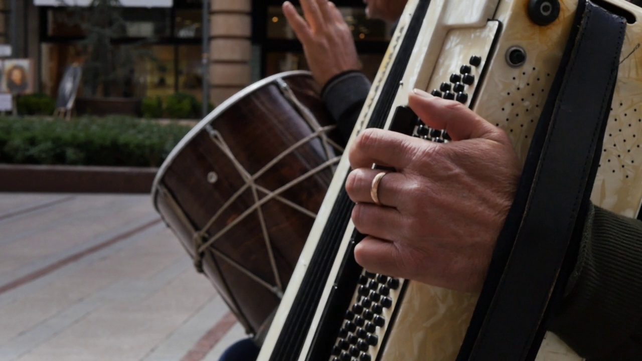 两名资深街头音乐家在城市的手风琴和鼓演奏慢动作。老年街头音乐家的二重唱。视频下载
