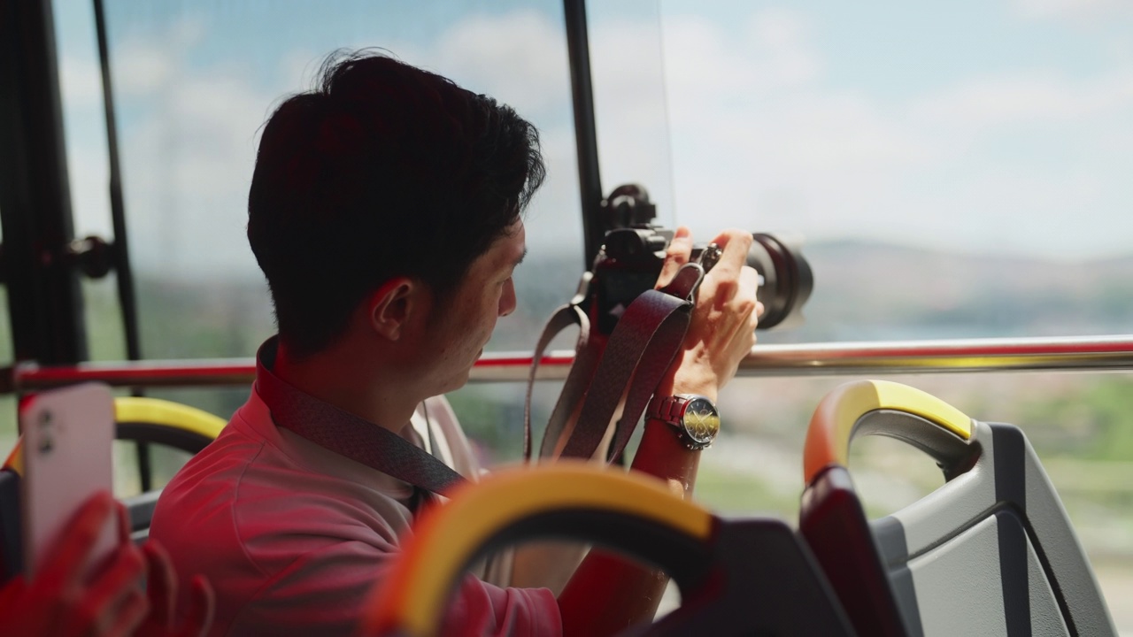 年轻男性游客乘坐城市旅游大巴，在旅途中拍摄照片和视频视频下载