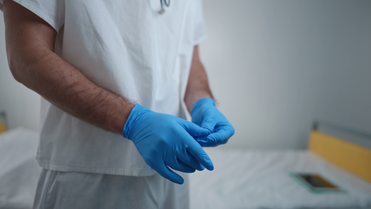 戴着蓝色一次性外科手套的面目全非的医生站在医院病房室内。身穿制服的高加索自信职业男子在诊所为病人检查做准备。视频素材