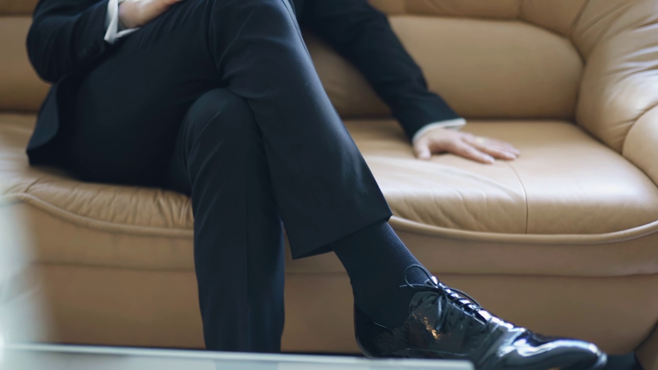 一个男人跷着二郎腿坐在沙发上。慢动作拍摄视频下载