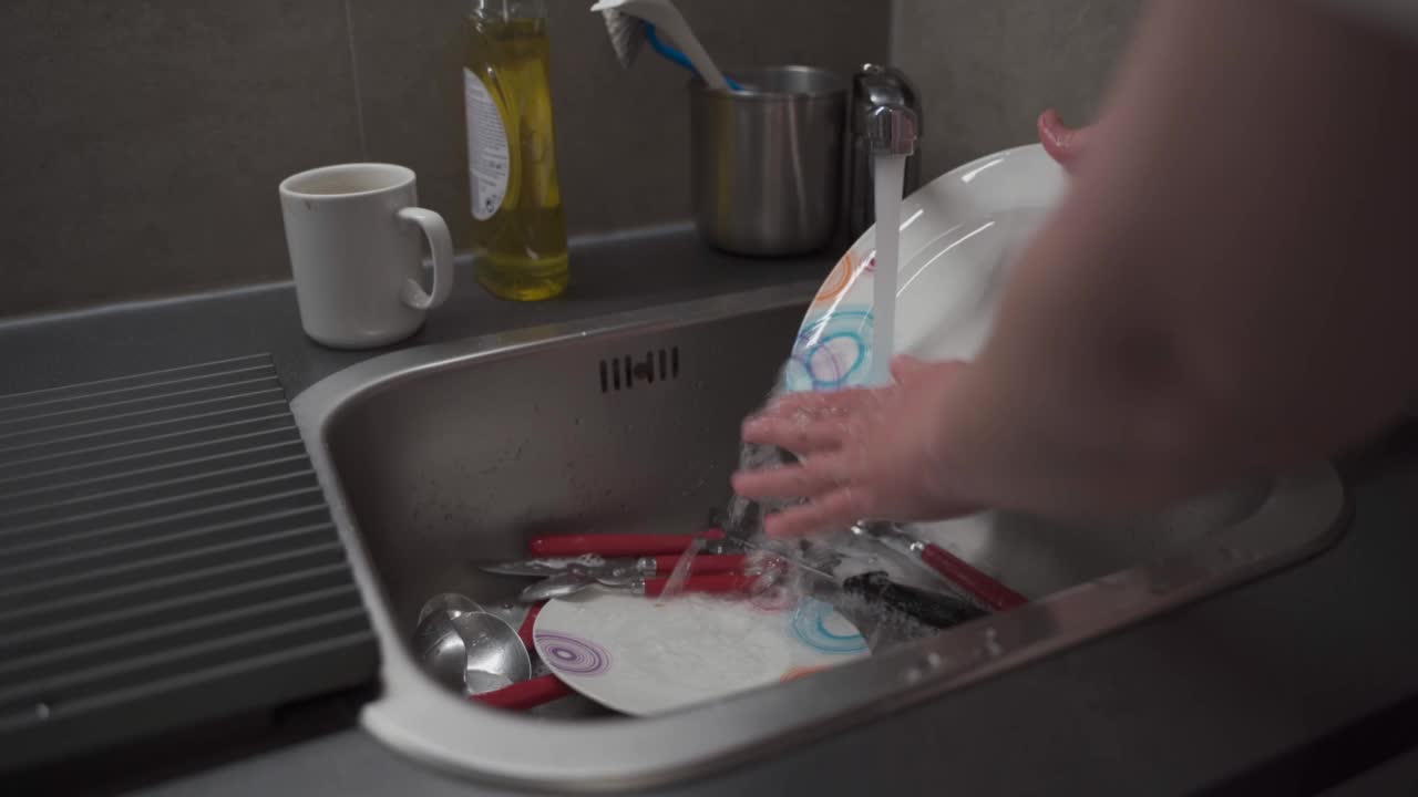 主妇女佣在厨房里洗碗。女人洗碗的双手。用清洁皂清洗盘子。女性用手在厨房的水槽里洗碗。家庭的概念视频素材