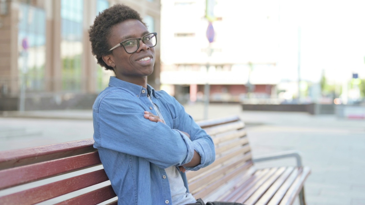 年轻的非洲男子坐在长凳上对着镜头微笑视频素材