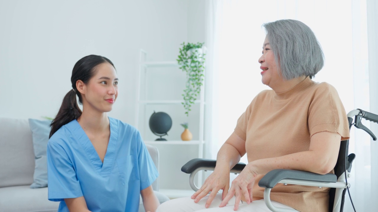 亚洲年轻的护理人员在家里照顾轮椅上的老年妇女。有吸引力的美丽的护士医生感觉快乐，同时谈论和支持老年，老年成熟的女性病人在养老院照顾。视频素材
