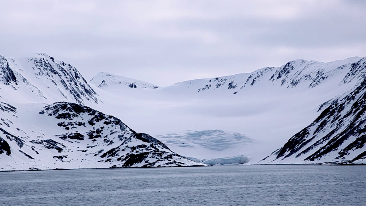 在挪威斯匹次卑尔根群岛的斯瓦尔巴群岛，蓝色的冰川在蓝天下平静的大海中流淌视频下载