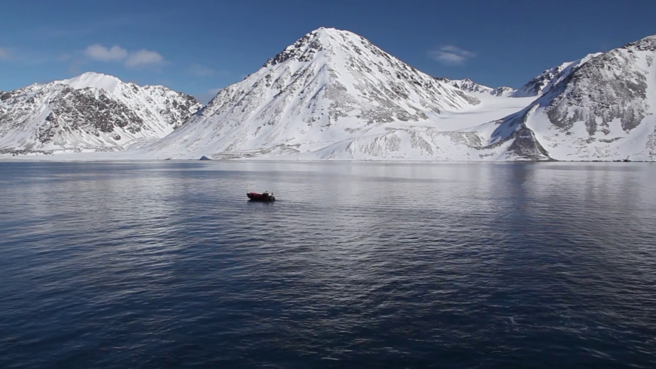 在挪威斯瓦尔巴群岛的斯匹次卑尔根群岛，一艘汽艇站在平静的海面上，蓝天下，雪山下视频下载