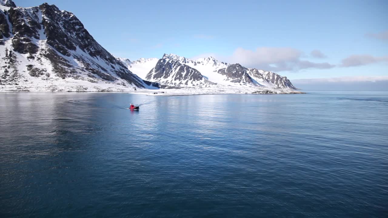 在挪威的斯匹次卑尔根群岛，在蓝天和雪山下，摩托艇在平静的海面上移动视频下载