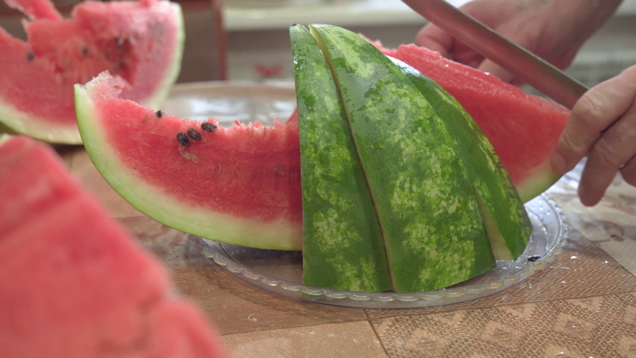 男人用刀把成熟的红西瓜切成块，放在盘子上。特写镜头。视频素材