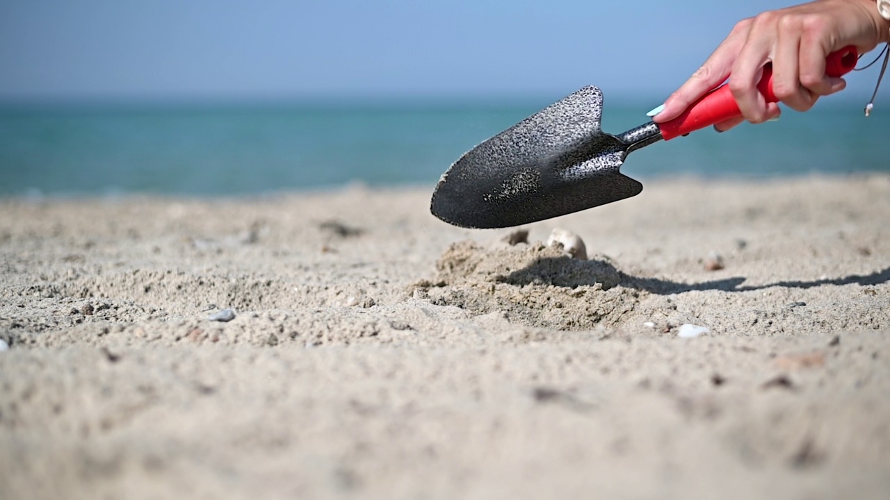 女子手用铁锹挖洞在沙滩上放太阳伞。慢动作视频素材