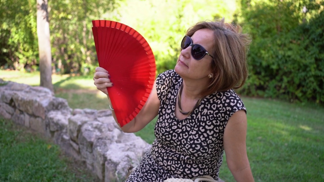 成熟的女人在酷暑中在公园里扇风。视频下载
