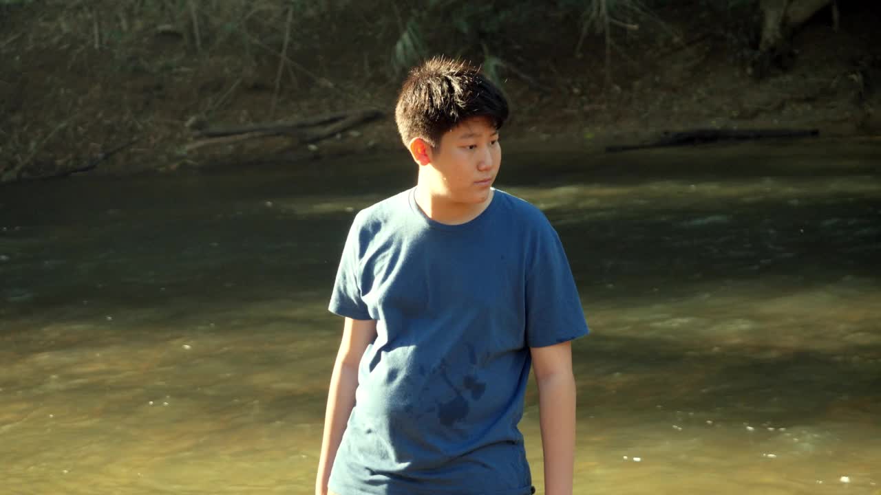 快乐的亚洲男孩在河流中放松，在阳光下的丛林，户外生活理念。视频素材