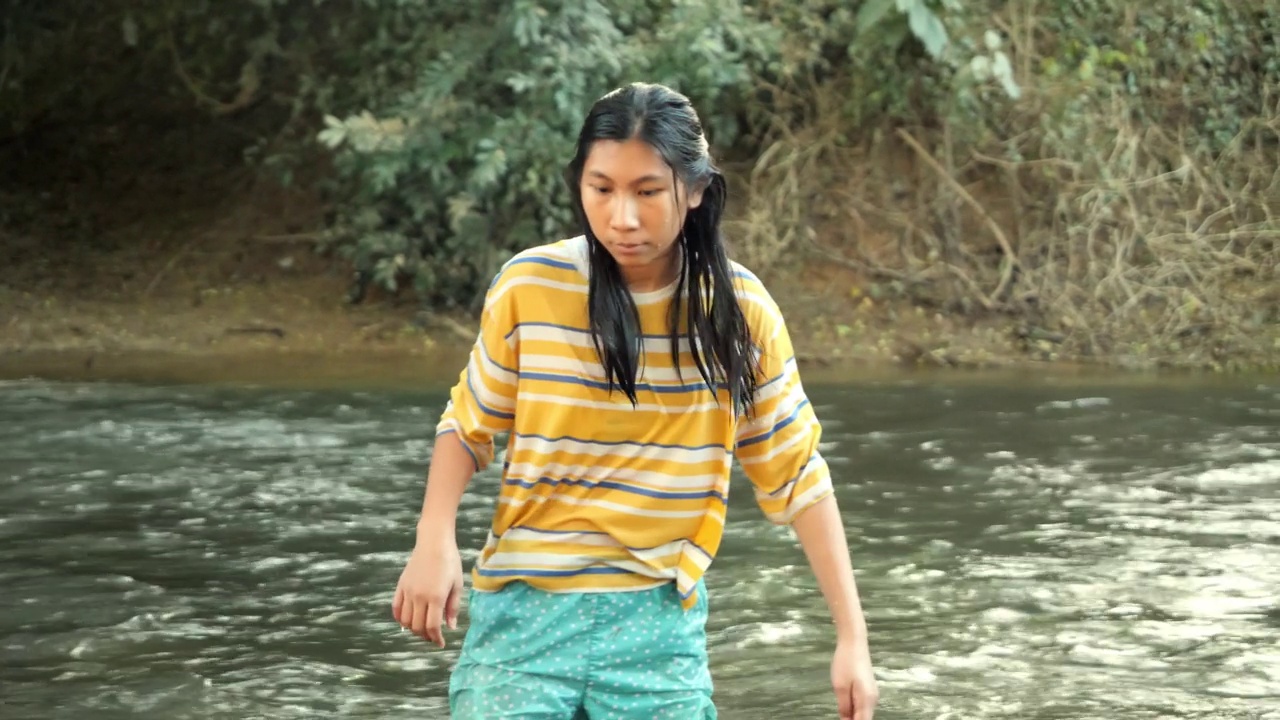 快乐的亚洲女孩放松在河流在阳光的丛林，户外生活理念。视频素材