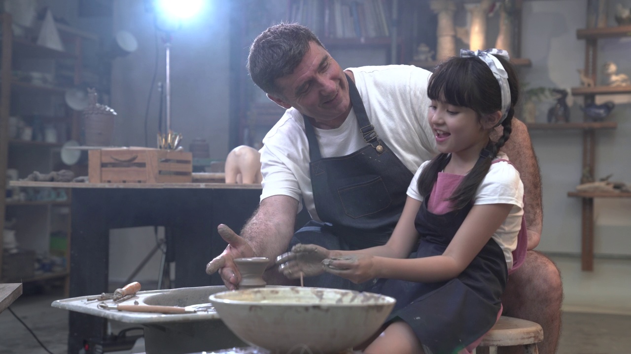 父亲和小女儿在作坊的陶轮上一起做陶器。视频下载