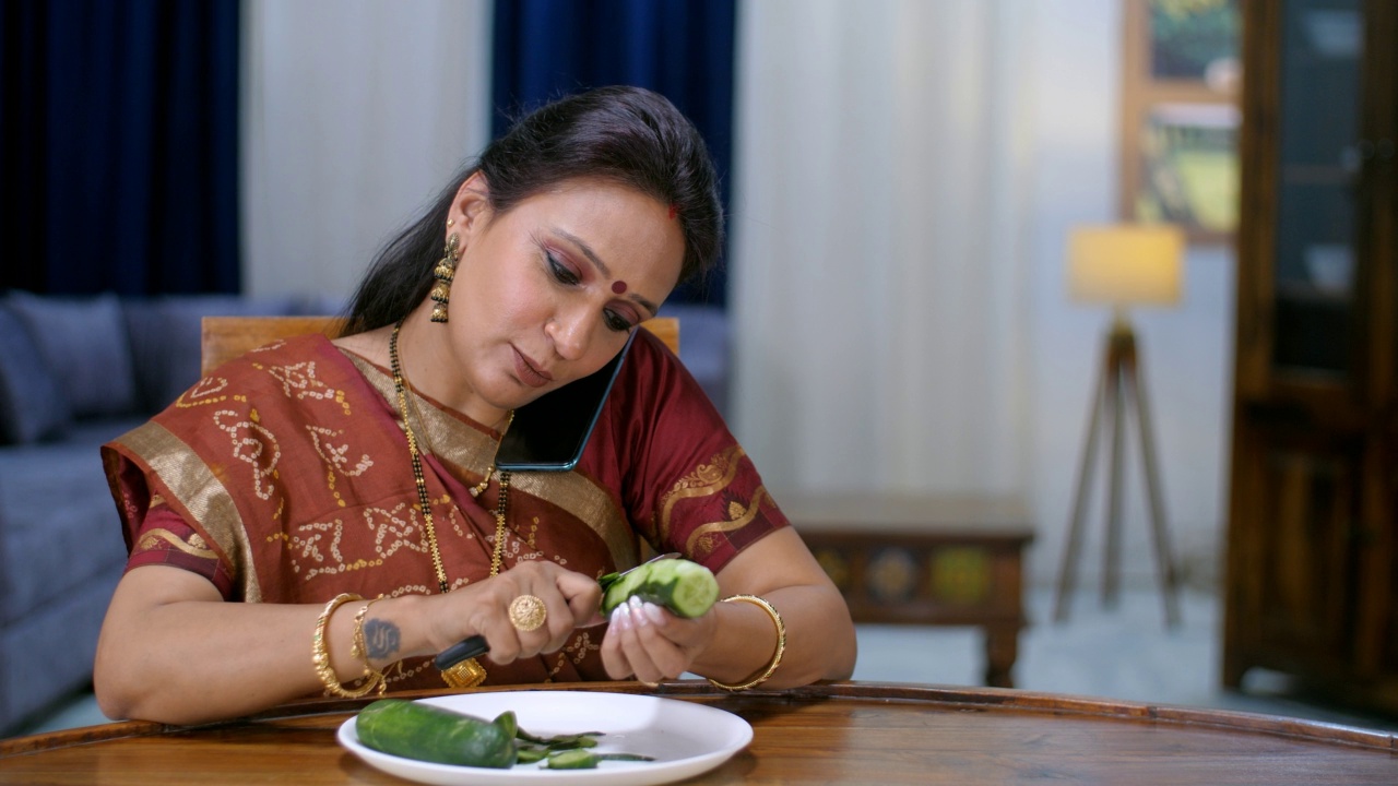一名中年印度家庭主妇一边切菜一边用智能手机聊天——这是家庭工作，家庭生活方式视频素材