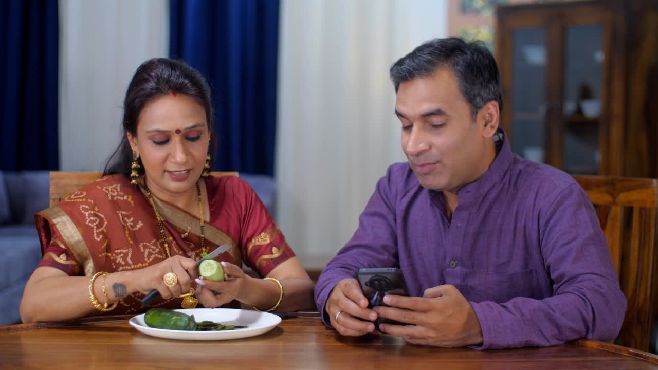一个中年印度家庭主妇在做家务，而她的丈夫在忙着打电话，这是一种家庭生活方式，休闲时间视频素材