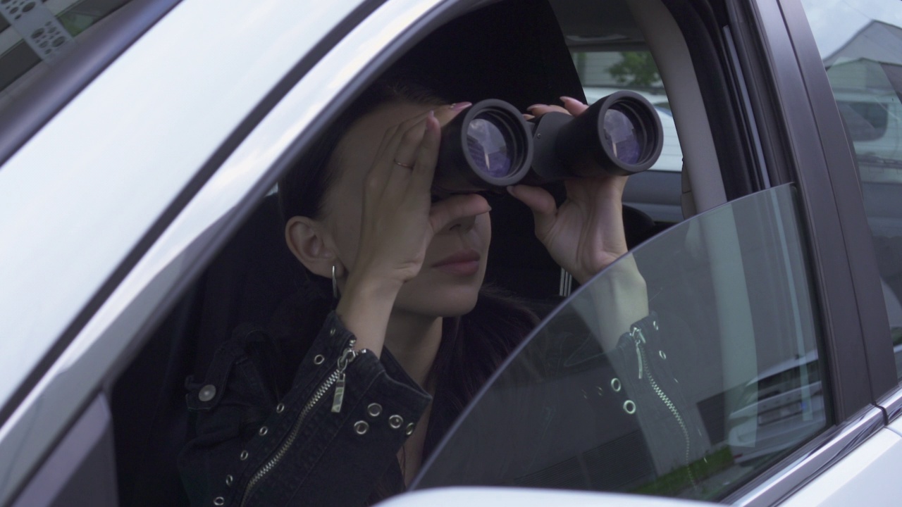 侦探坐在车里，透过望远镜看公寓大楼。特写镜头视频下载
