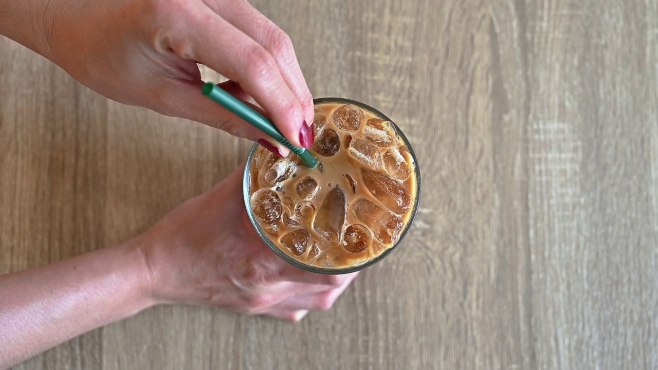 饮用前用吸管搅拌冰咖啡的桌面视图。视频下载
