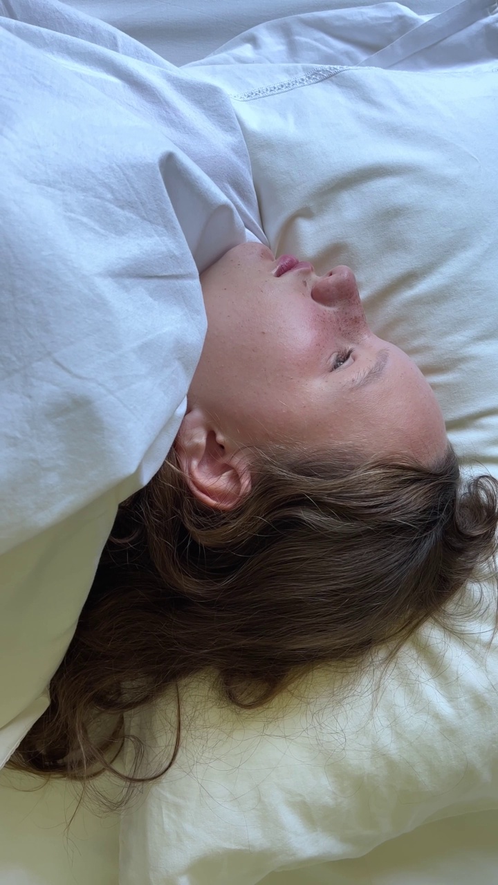 垂直视频有雀斑的少女在她的床上睡着了，她的眼睛闭上，她陷入了一个梦，可以用来广告床上的亚麻或任何健康产品视频下载