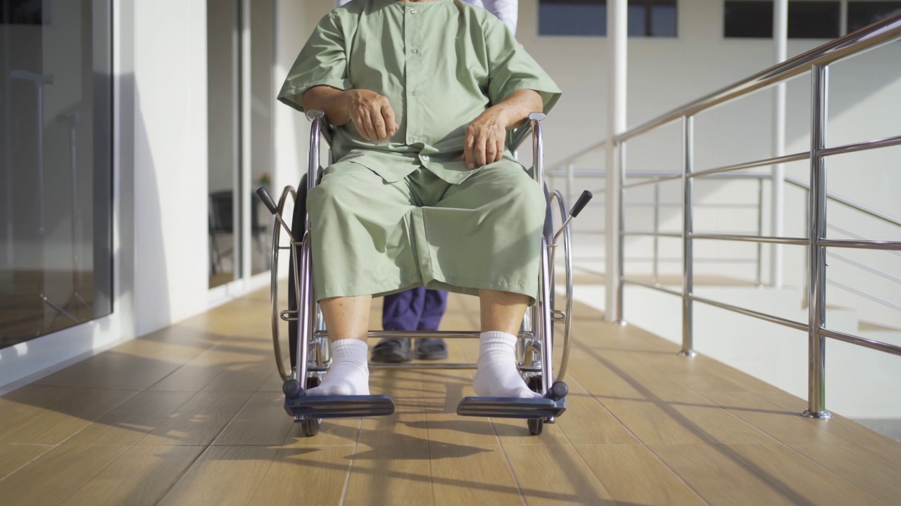 年迈的亚洲残疾病人或养恤金领取者和医生使用轮椅在医院的养老院练习行走。老年人生活方式、活动、娱乐。保健理疗视频素材