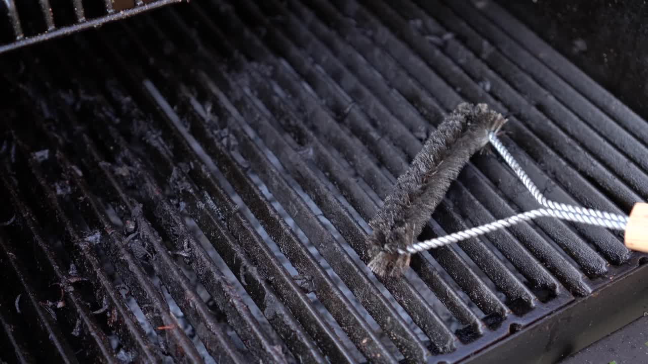 男子用金属刷清洁铁制烧烤格栅做饭后。把烧烤的维护视频素材