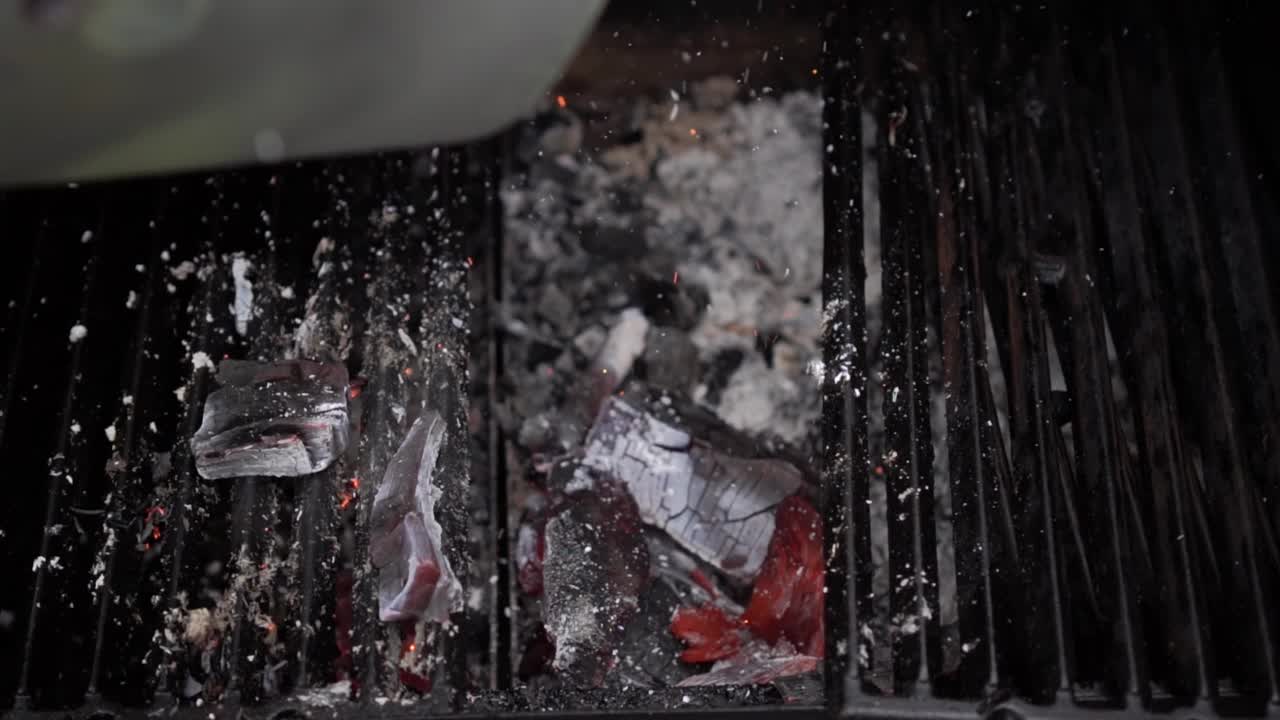 把烧热的木炭倒进烧烤架。烧红的铁制炉排上余烬燃烧。烧烤准备视频素材