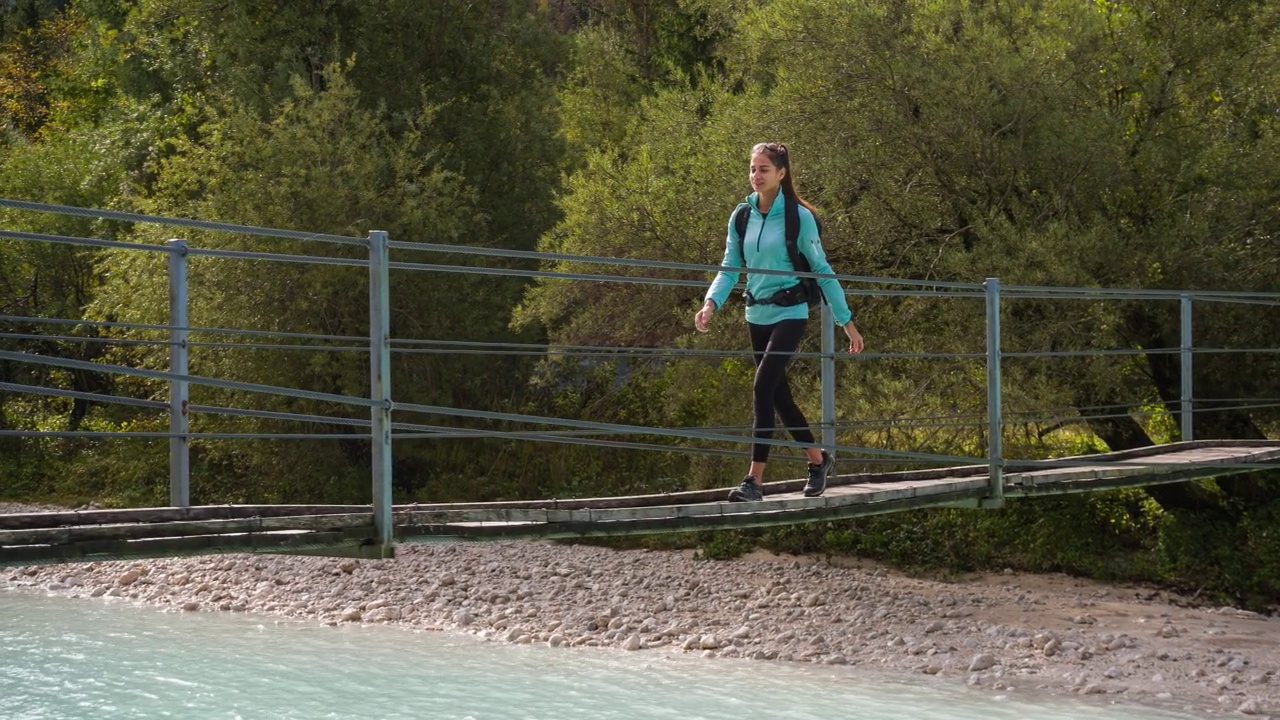 一个年轻的女游客徒步穿越山河上的木桥的移动镜头视频素材