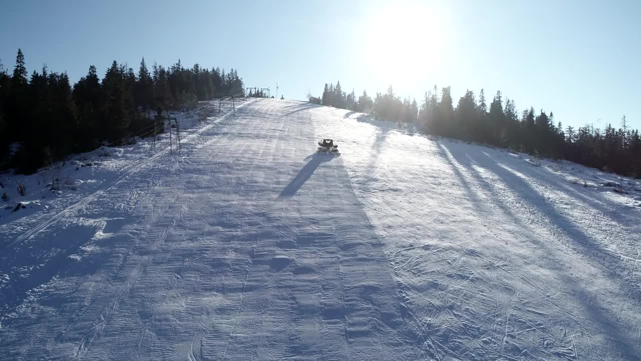 在冬季滑雪场的斜坡上，从空中俯视雪地摩托或雪地美容师视频下载
