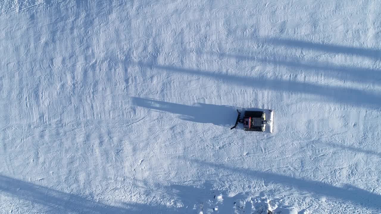 在冬季滑雪场的斜坡上，从空中俯视雪地摩托或雪地美容师视频下载